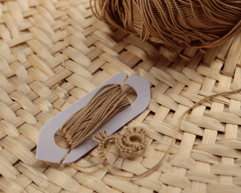 DIY tatting shuttle made from a plastic card with thread wound around it and a tatting project in progress