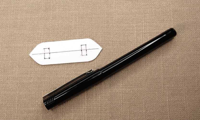 White plastic shuttle shape with marked points for holes, next to a fine marker