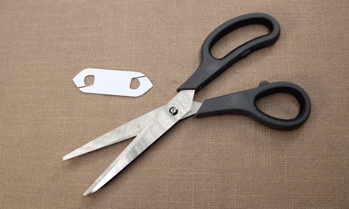 Plastic shuttle shape with small angled notches cut, next to scissors