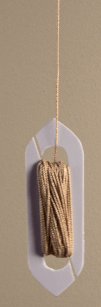 Plastic tatting shuttle with thread wound around it, hanging freely