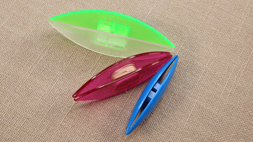 Three colourful post tatting shuttles from different brands — Starlit, Lacis, and Prym — with a small amount of thread wound on one shuttle.