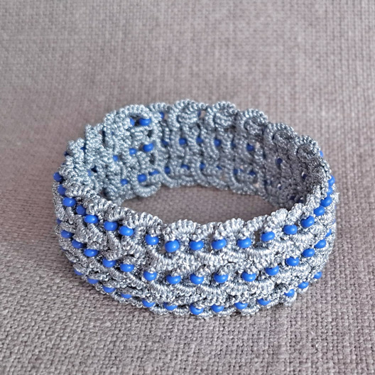 Full view of a silver knitted tatting bracelet adorned with blue beads, showcasing its intricate lace pattern.