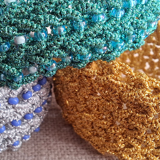 Close-up of three handmade tatted bracelets in different colors, including one without beads, showing thread texture and stitch detail.