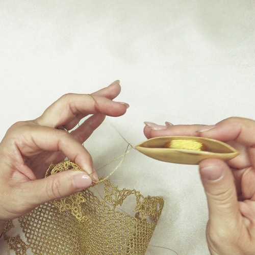 Hands tatting a lace doily using shuttle tatting with gold thread
