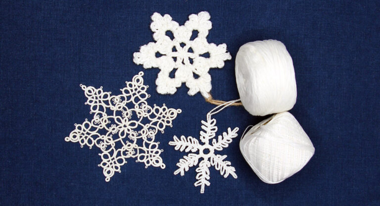 Three white snowflakes on white background with two balls of white thread; left is tatting snowflake by Alicia (design "Miranda" by Renata Niemczyk), middle and right are crochet snowflakes by Maya Milarski and Helena Kozłowska.